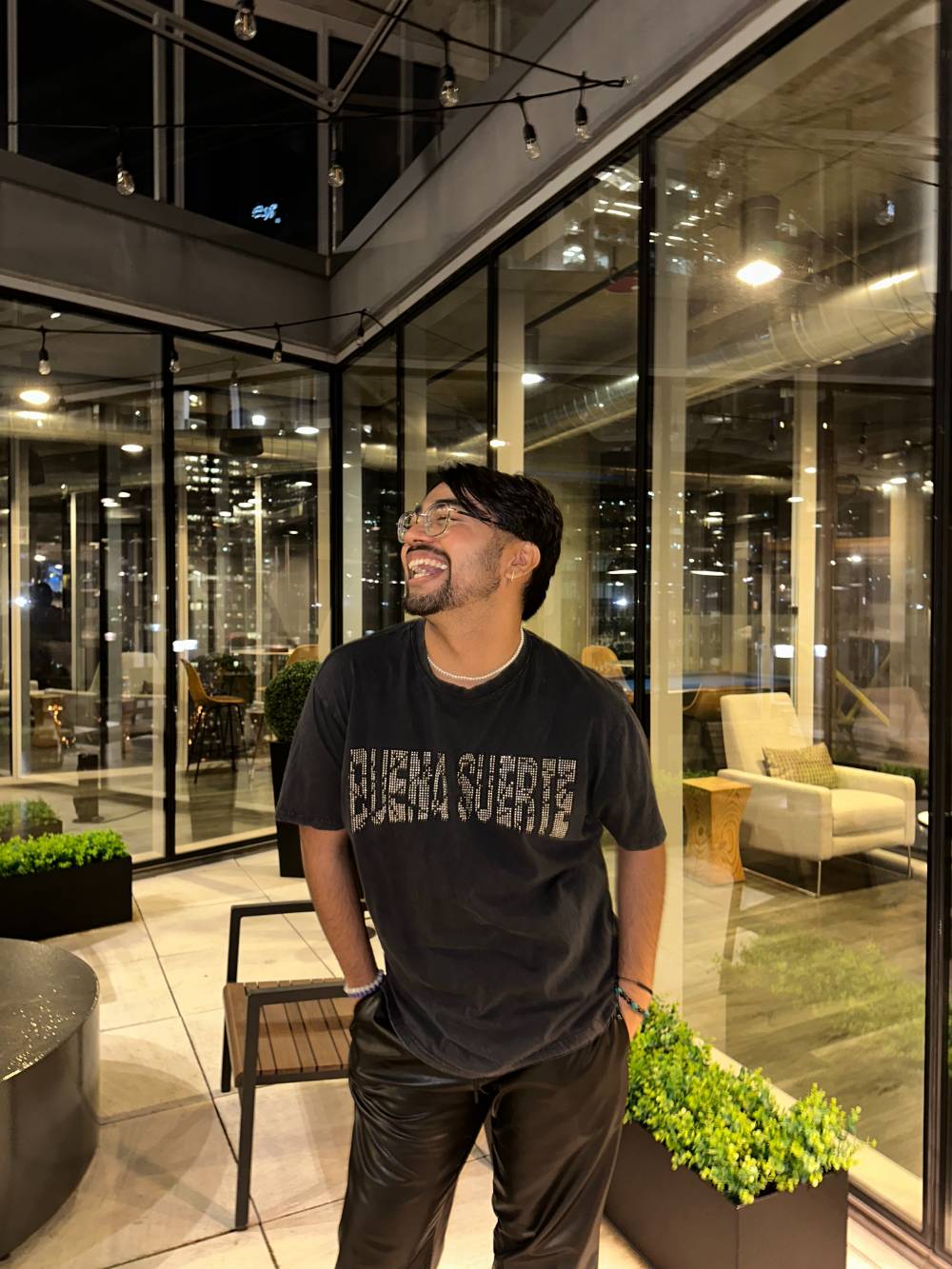 Image 1 of 2 Photo of male student standing in front of windows with hands in pockets and laughing